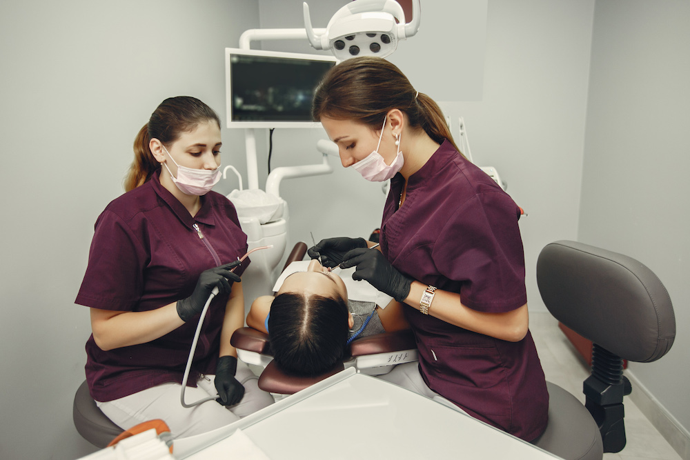 The dentist treats the girl's teeth. A young woman visited a dentist. The doctor works with an assistant